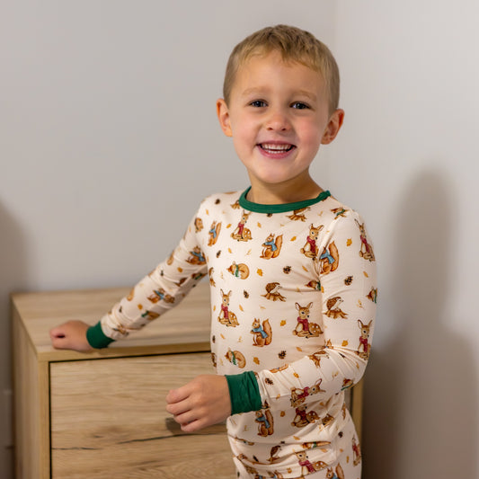 Child wearing pajamas with animal print standing next to a wooden nightstand.