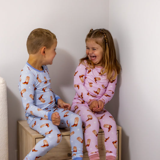 Two children in pajamas sitting on a wooden box against a white wall.