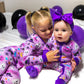 Two children in Halloween-themed pajamas surrounded by balloons on a bed.