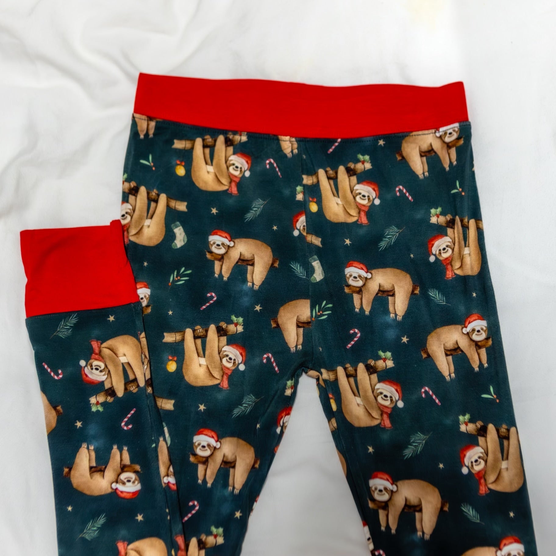 Pajama pants with sloth pattern and red cuffs on a white background